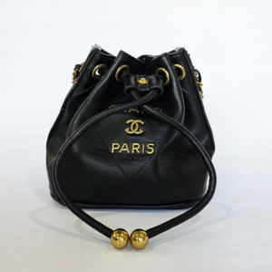 Pre-loved black bucket bag featuring a quilted lower panel, gold lettering, and a drawstring closure with gold balls.