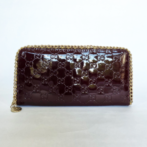 Pre-loved glossy burgundy patent clutch wallet featuring an embossed monogram pattern and gold chain edge.