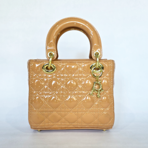 Pre-loved nude camel patent top-handle bag featuring geometric quilting, gold hardware, and a hanging R charm.